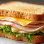 A Turkey Cheese Sandwich with layers of freshly sliced turkey, melted cheese, and toasted bread, served with chips and fresh lettuce.